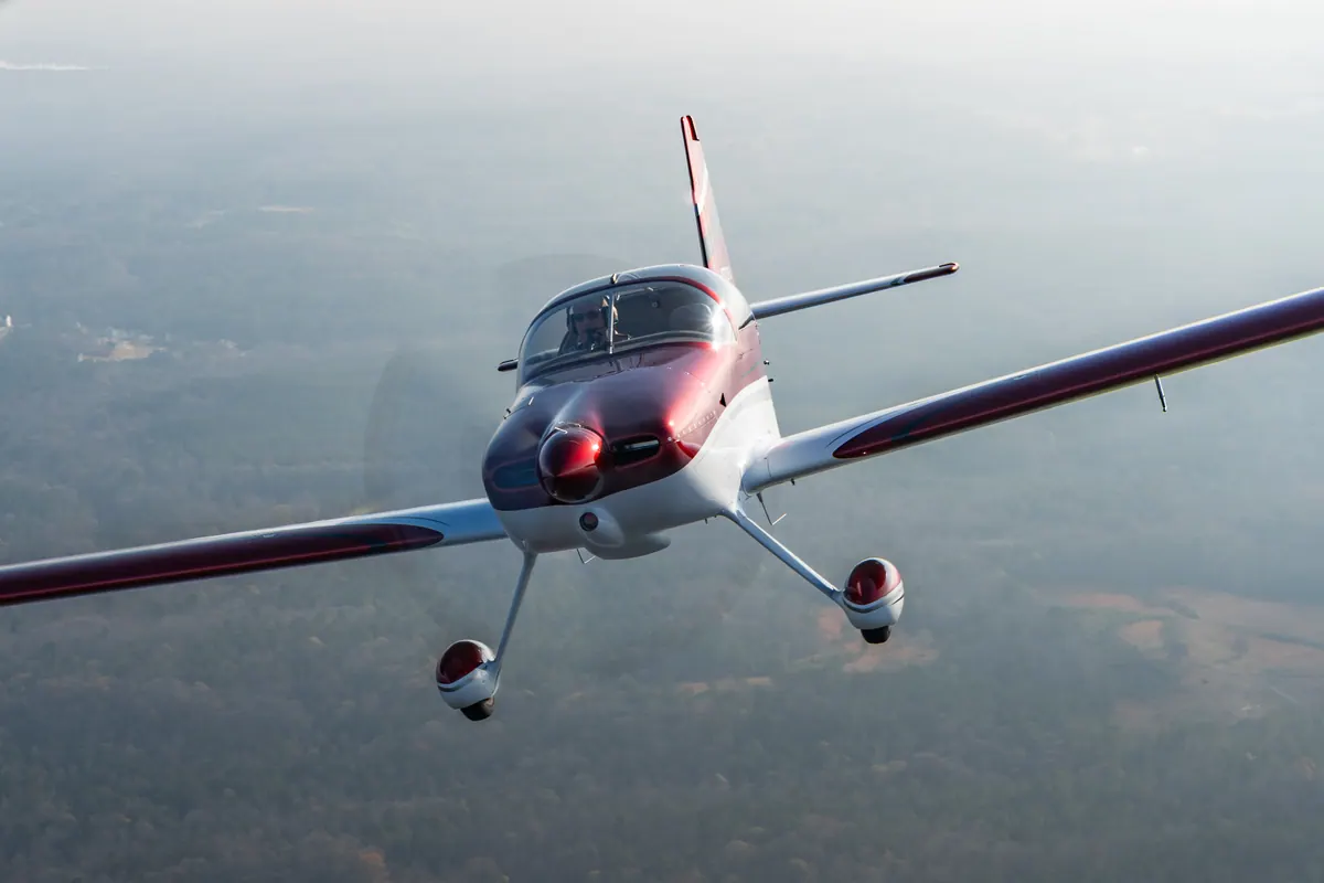 The red-and-white low-wing homebuilt banks toward the camera, filling the frame against hazy countryside