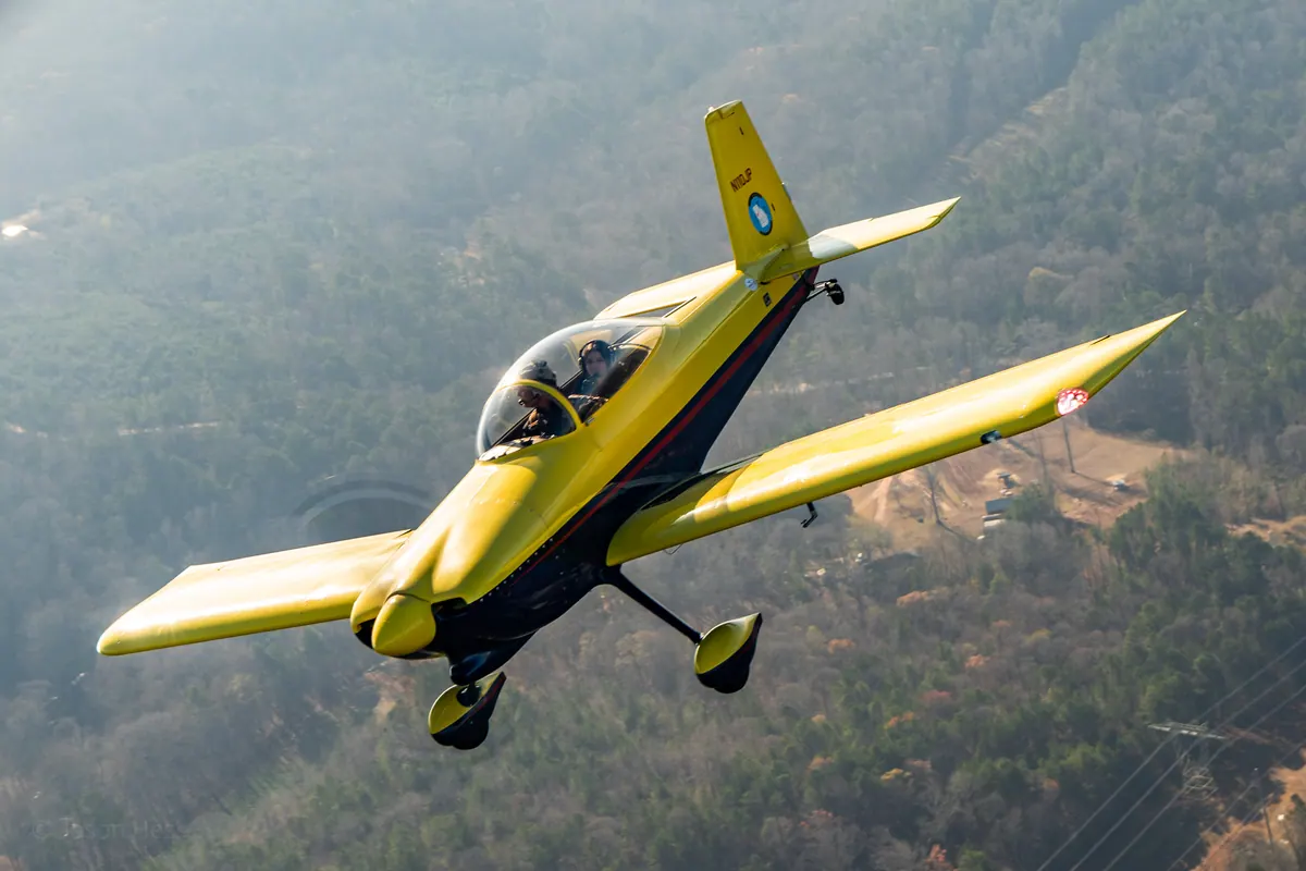 Close view of the yellow low-wing homebuilt banking steeply toward the camera over hazy hills