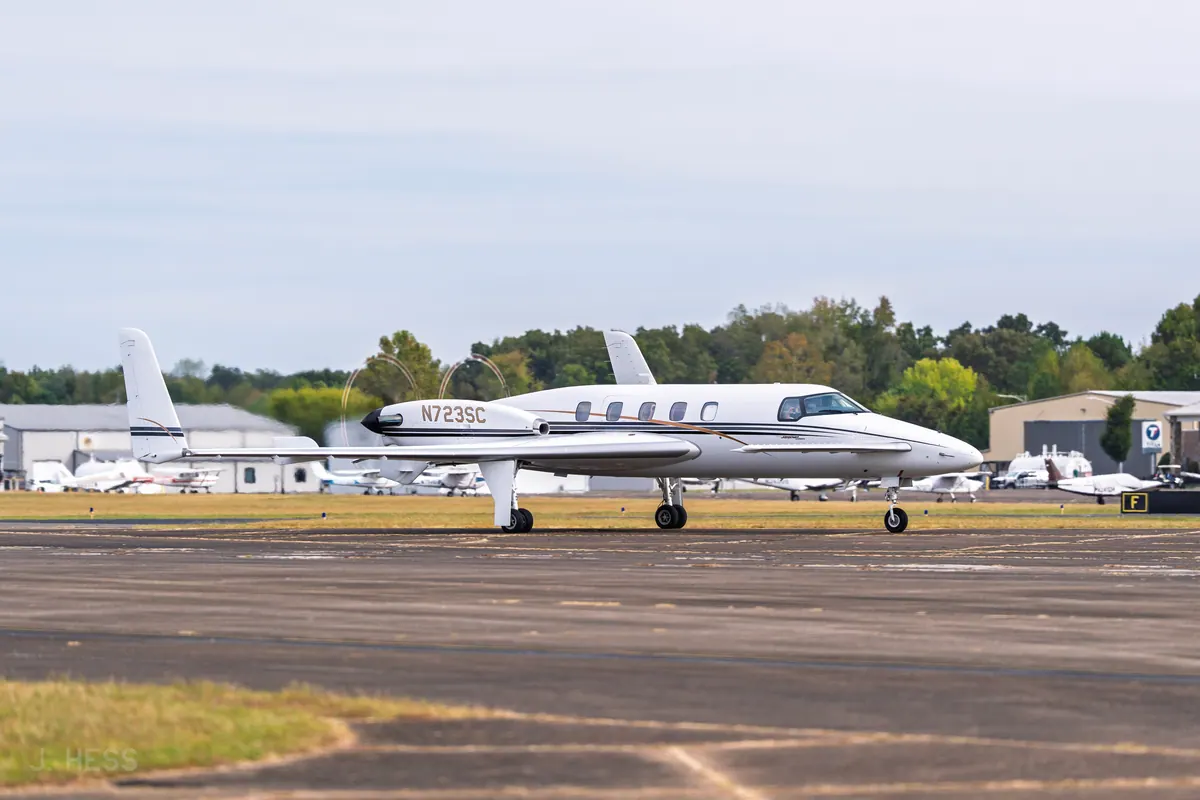A white Beechcraft Starship with its distinctive canard and pusher propellers taxiing past hangars