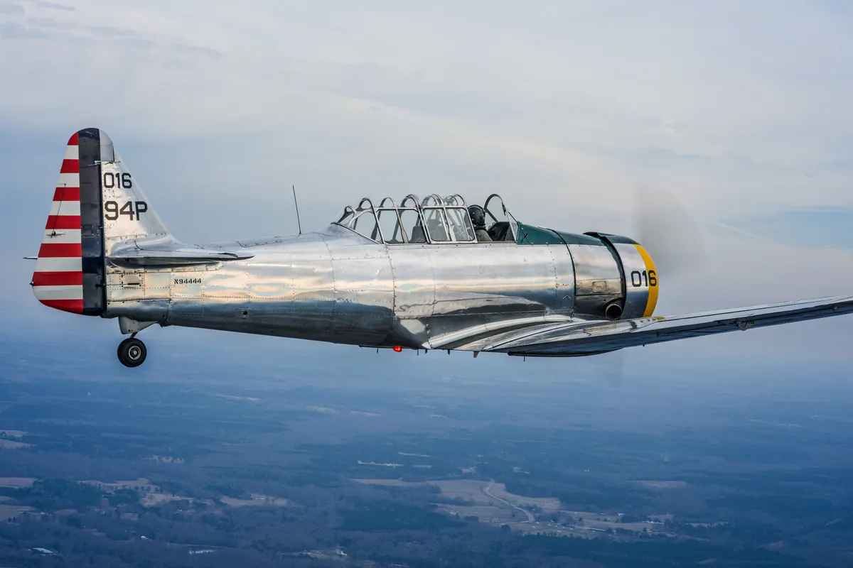 Close side view of the polished silver trainer '016' flying level above hazy blue countryside