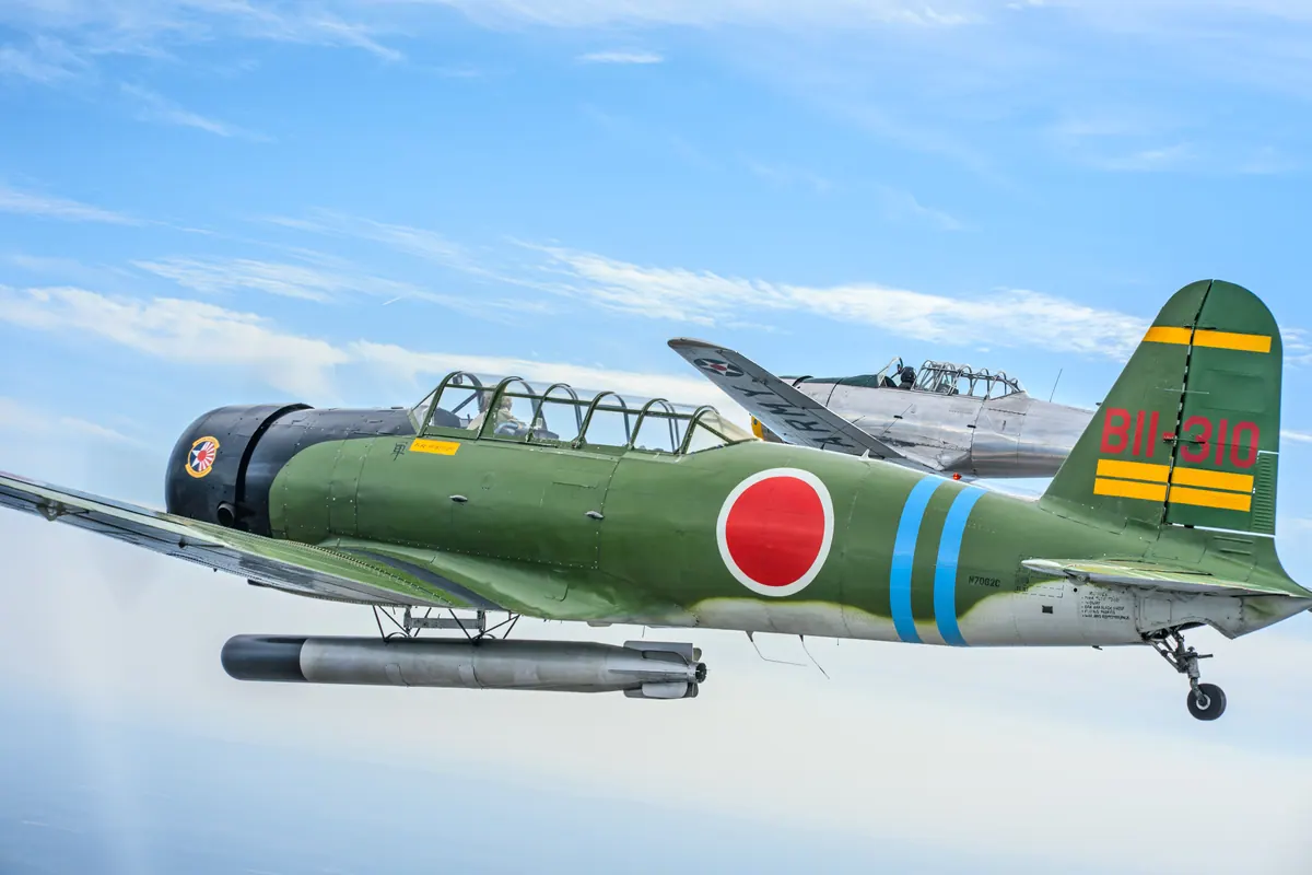 The green 'Kate' torpedo-bomber replica flies in front of the silver trainer against a sky streaked with high cloud