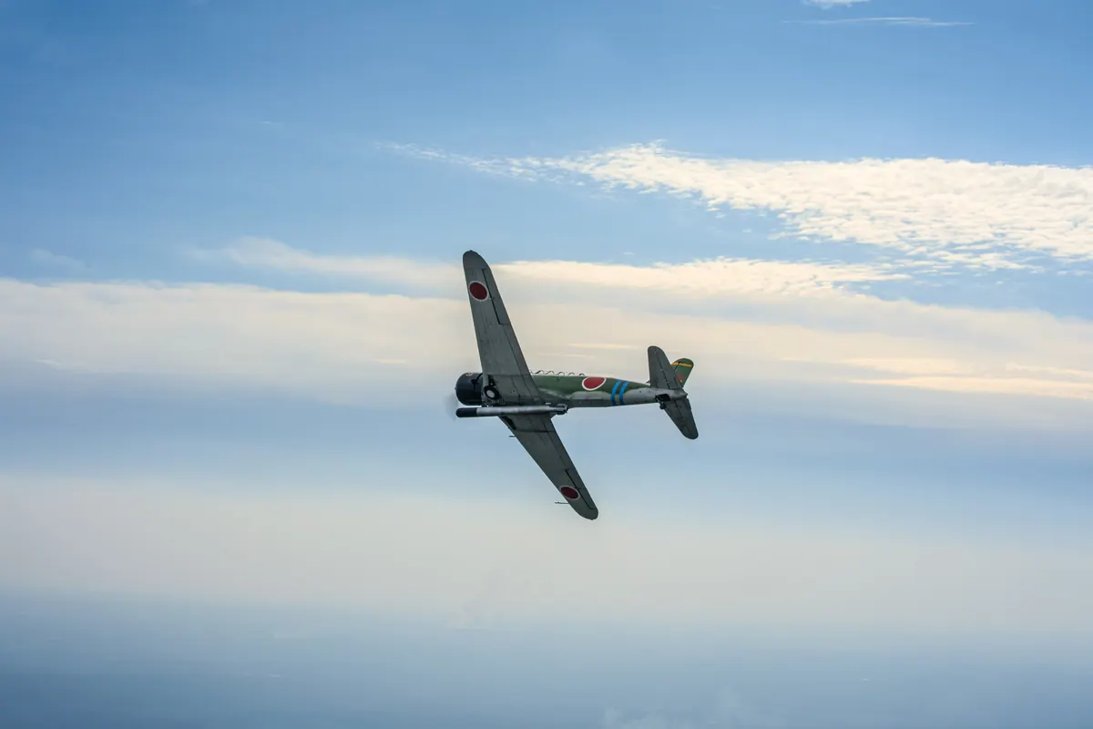 The green 'Kate' torpedo-bomber replica banks away against blue sky and wispy cloud