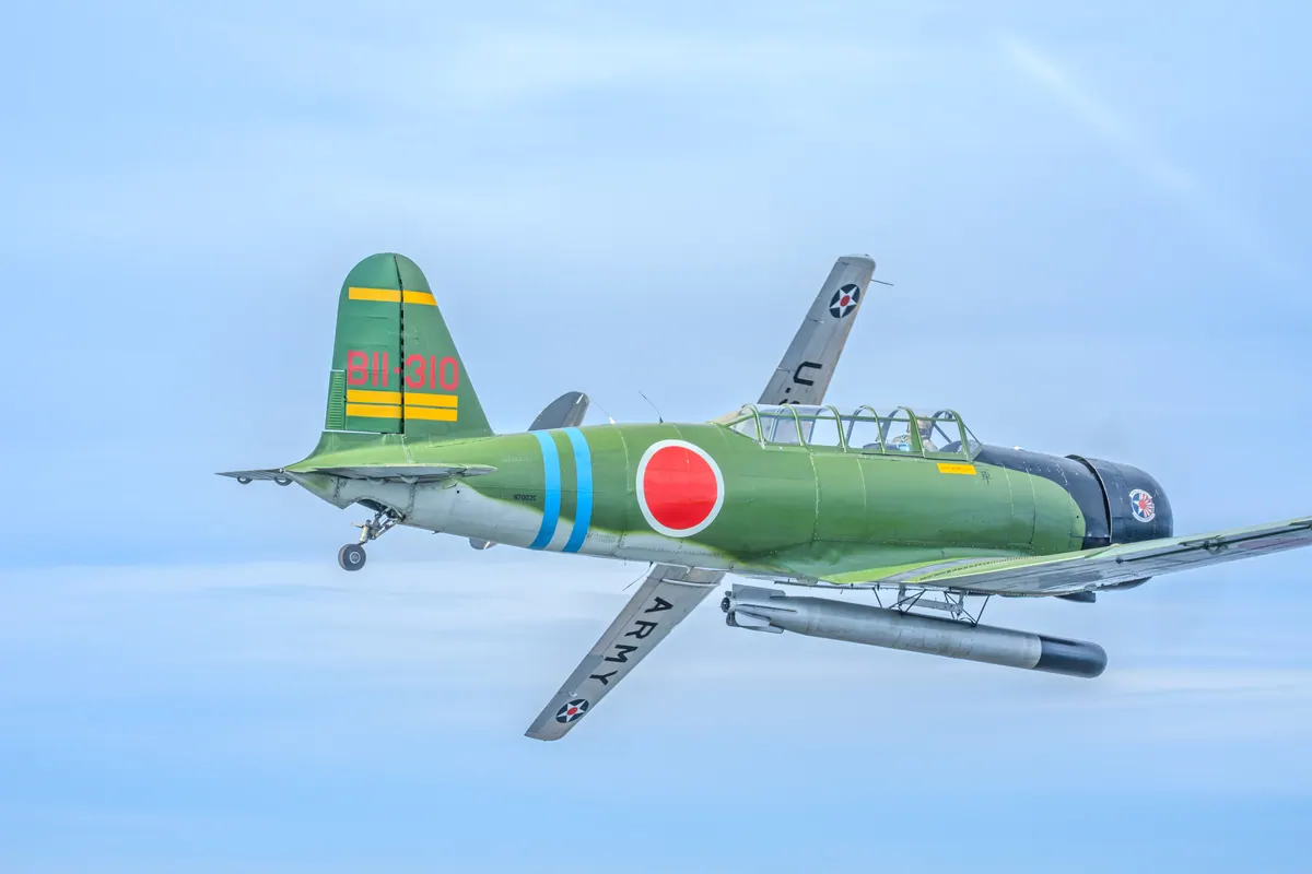 The green 'Kate' torpedo-bomber replica with the silver trainer banking behind it against a clear blue sky
