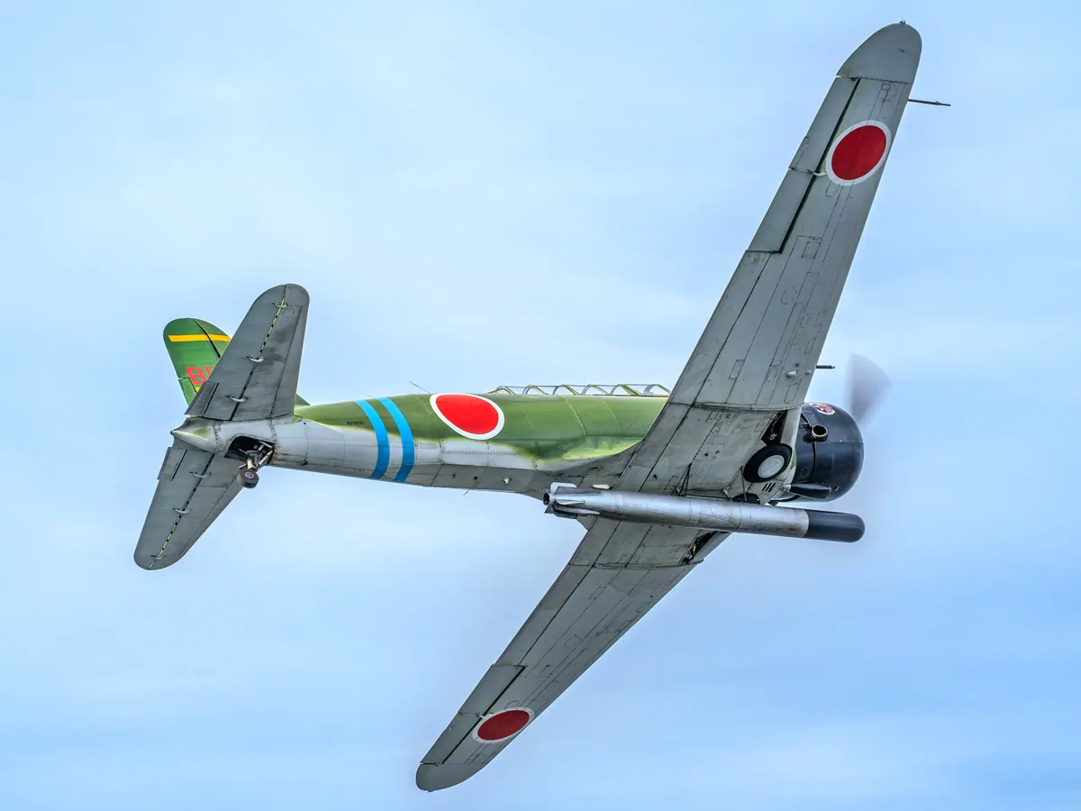 The green 'Kate' torpedo-bomber replica banks hard, showing the red roundels under its wings and the torpedo beneath