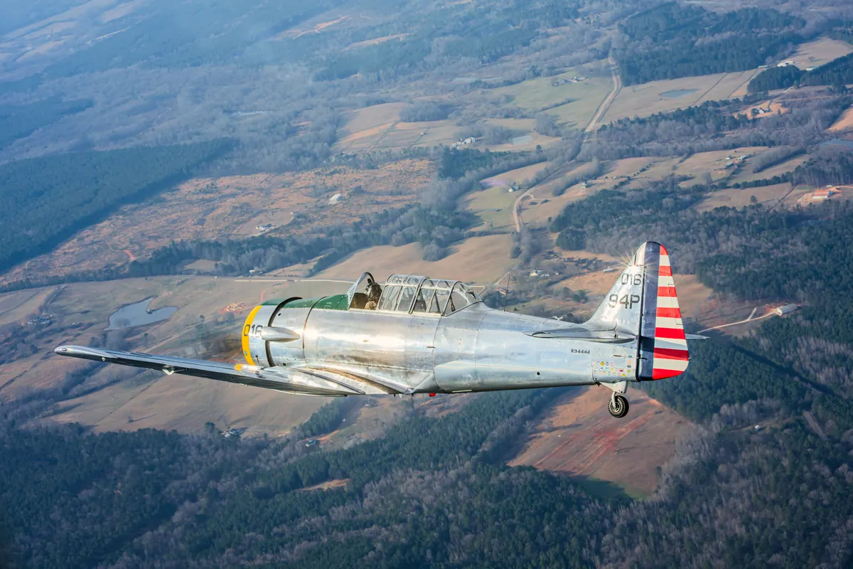 The polished silver trainer '016' flies over red-clay fields and pine woods seen from above