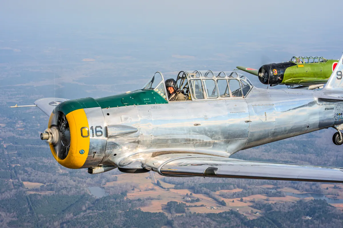 Tight view of the yellow-cowled nose and canopy of the silver trainer, with the green 'Kate' torpedo-bomber replica just behind