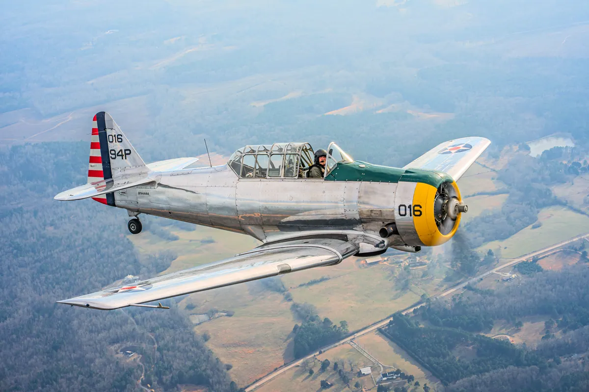 The polished silver trainer '016' banks toward the camera, seen from above against fields and roads