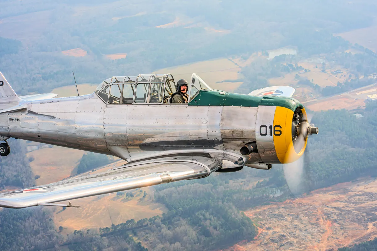 Tight view of the polished silver trainer '016', propeller a blur, over red-clay fields