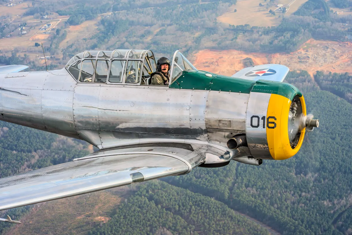 Tight view of the silver trainer's fuselage and canopy over wooded hills