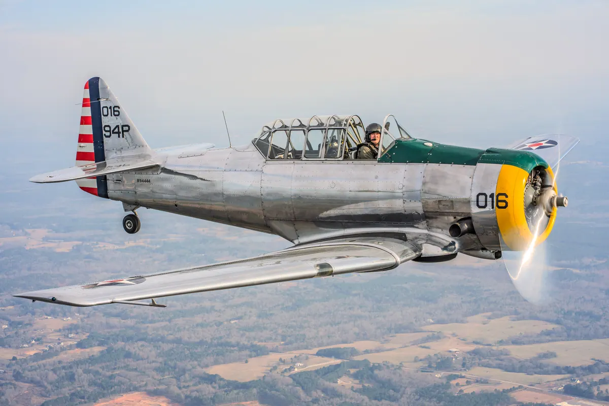 The polished silver trainer '016' flying right, vapour trailing from its propeller tips