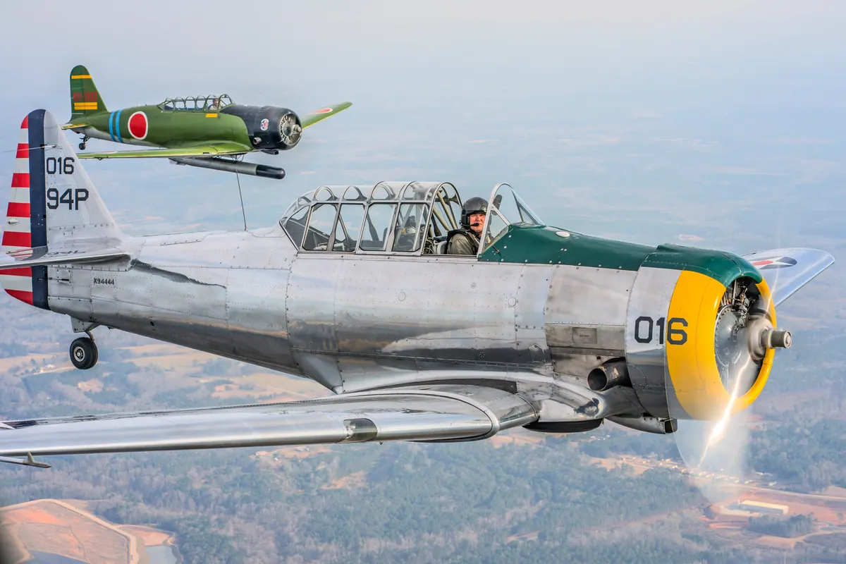 The polished silver trainer '016' with the green 'Kate' torpedo-bomber replica high and behind it, vapour off the propeller