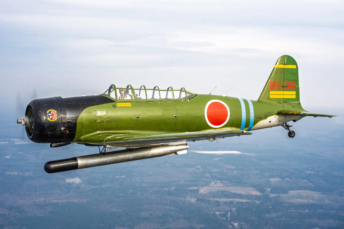 The green 'Kate' torpedo-bomber replica flies left across a hazy gray landscape