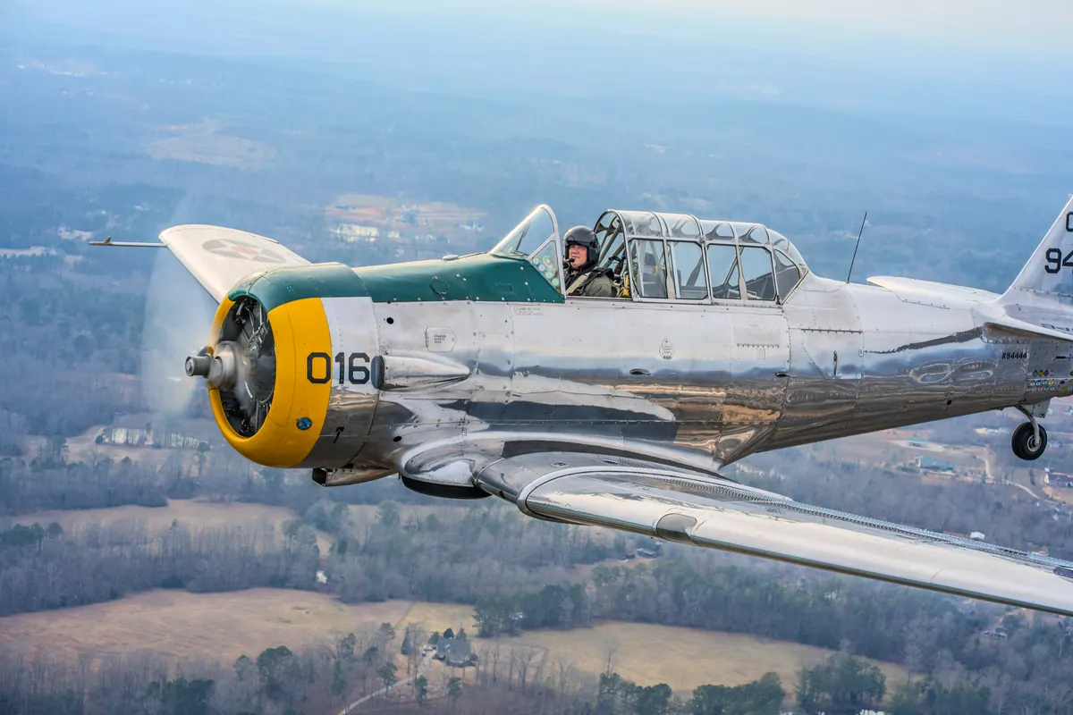 Tight view of the silver trainer's yellow nose and canopy over wooded country